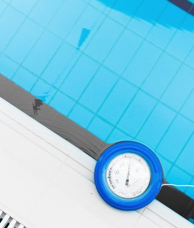 Floating thermometer measuring cold water temperature in a blue pool